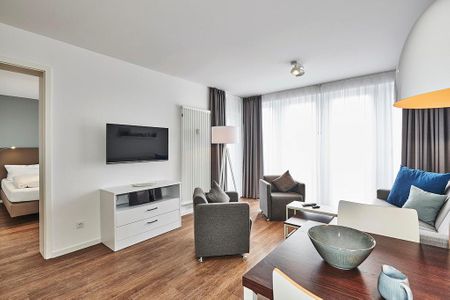 Deichhäuser Anna Küste Deichhäuser Anna Küste 4-34 Bensersiel - Wohn-Essbereich mit Couch, Flatscreen TV, Esstisch, Sitzgelegenheit und Zugang zum Balkon