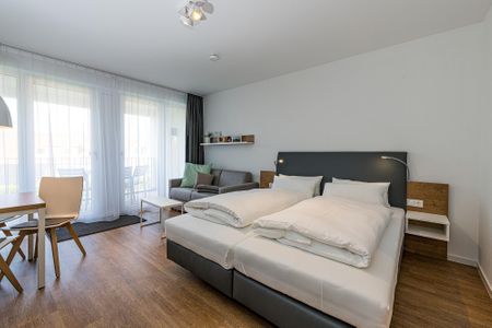 Deichhäuser Anna Küste Deichhäuser Anna Küste 8-22 Bensersiel - Wohn-Ess-Schlafbereich mit Sofa, Esstisch, Sitzgelegenheit und Doppelbett sowie Zugang zum Balkon