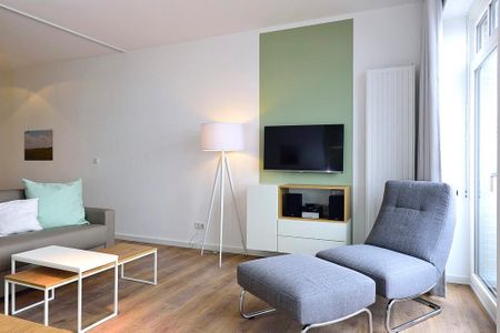 Aparthotel Anna Düne Aparthotel Anna Düne 1-21 Wangerooge - Wohn/ Essbereich mit Sessel und Fernseher