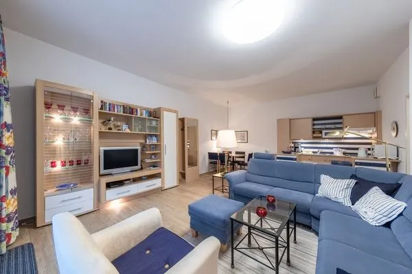 Ferienwohnung Bernstein Zingst – Großzügiges Wohnzimmer mit blauer Eckcouch, Vitrine, TV-Wand und offener Küche  Bernstein