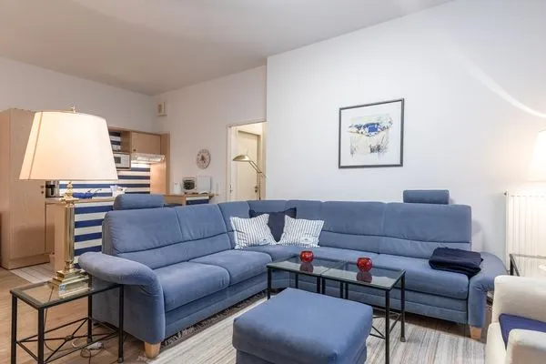 Ferienwohnung Bernstein Zingst – Gemütliches Wohnzimmer mit großer blauer Eckcouch, Glas-Couchtischen und maritimer Deko  Bernstein