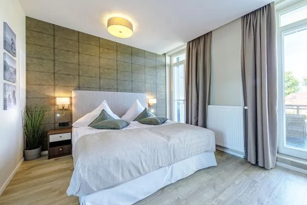 Ferienwohnung First Garden View Wustrow – modernes Schlafzimmer mit Boxspringbett und Zugang zum Balkon  First Garden View
