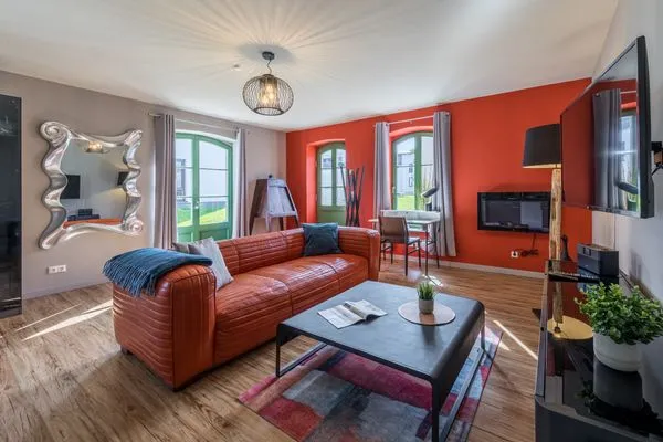 Ferienwohnung Müritzperle Klink - Wohnzimmer mit rotem Sofa und modernem Spiegel  Müritzperle