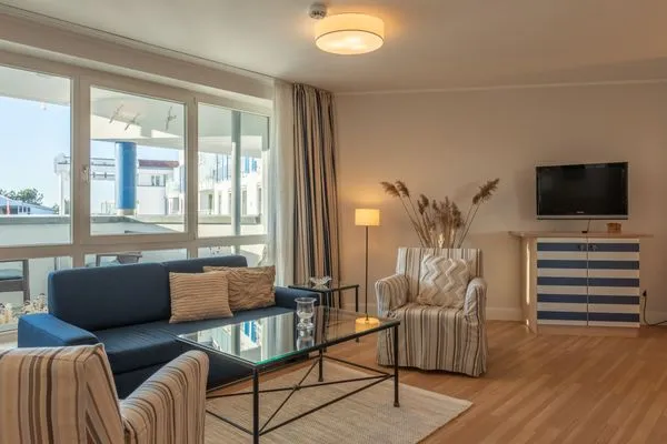 Ferienwohnung Kranichtanz Aparthotel Zingst - Blick ins helle Wohnzimmer mit einer Couch, zwei Sesseln und einem TV  Kranichtanz
