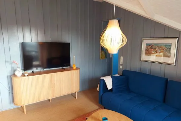 Wohnzimmer mit Couch, TV, Kamin und großen Fenstern  Immi's Hus