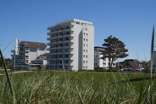 Hohe Gräser vor dem Gebäude Pacific Duhnen, das eine exponierte Lage am Strand von Cuxhaven mit Meerblick hat.  Haus Pacific Duhnen Nr. 91