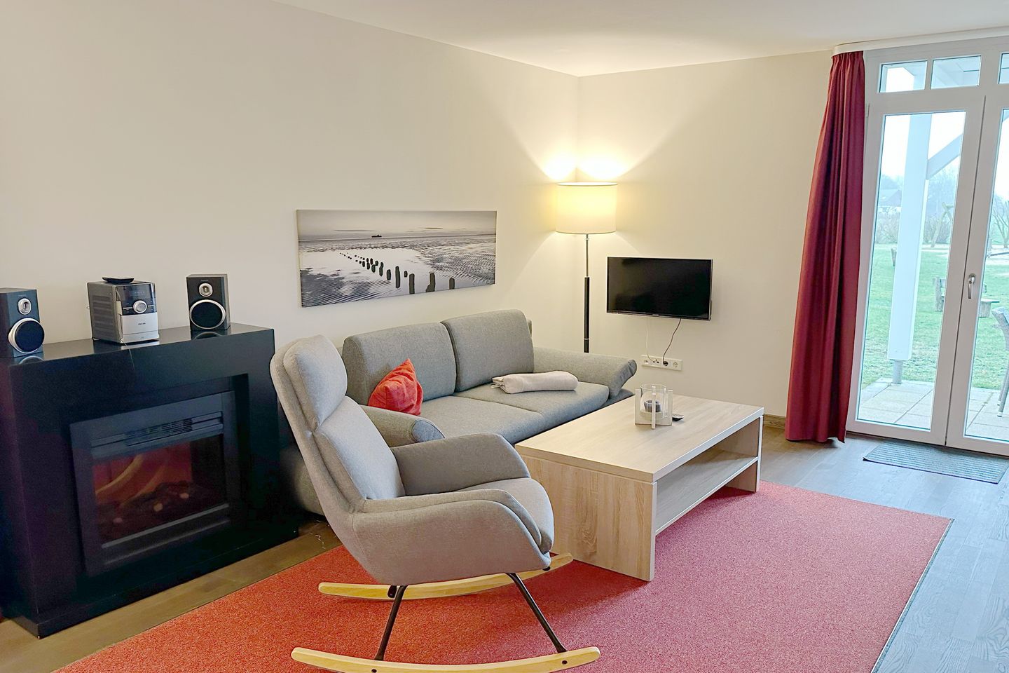 Resort Deichgraf Resort Deichgraf 27-01 Wremen - Wohnbereich mit Couch, Schaukelstuhl, Elektrokamin, Flatscreen TV und Zugang zur Terrasse