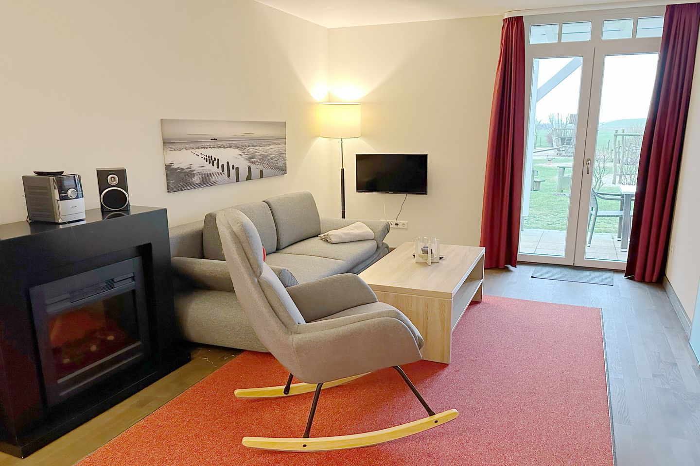 Resort Deichgraf Resort Deichgraf 27-01 Wremen - Wohnbereich mit Couch, Schaukelstuhl, Elektrokamin, Flatscreen TV und Zugang zur Terrasse