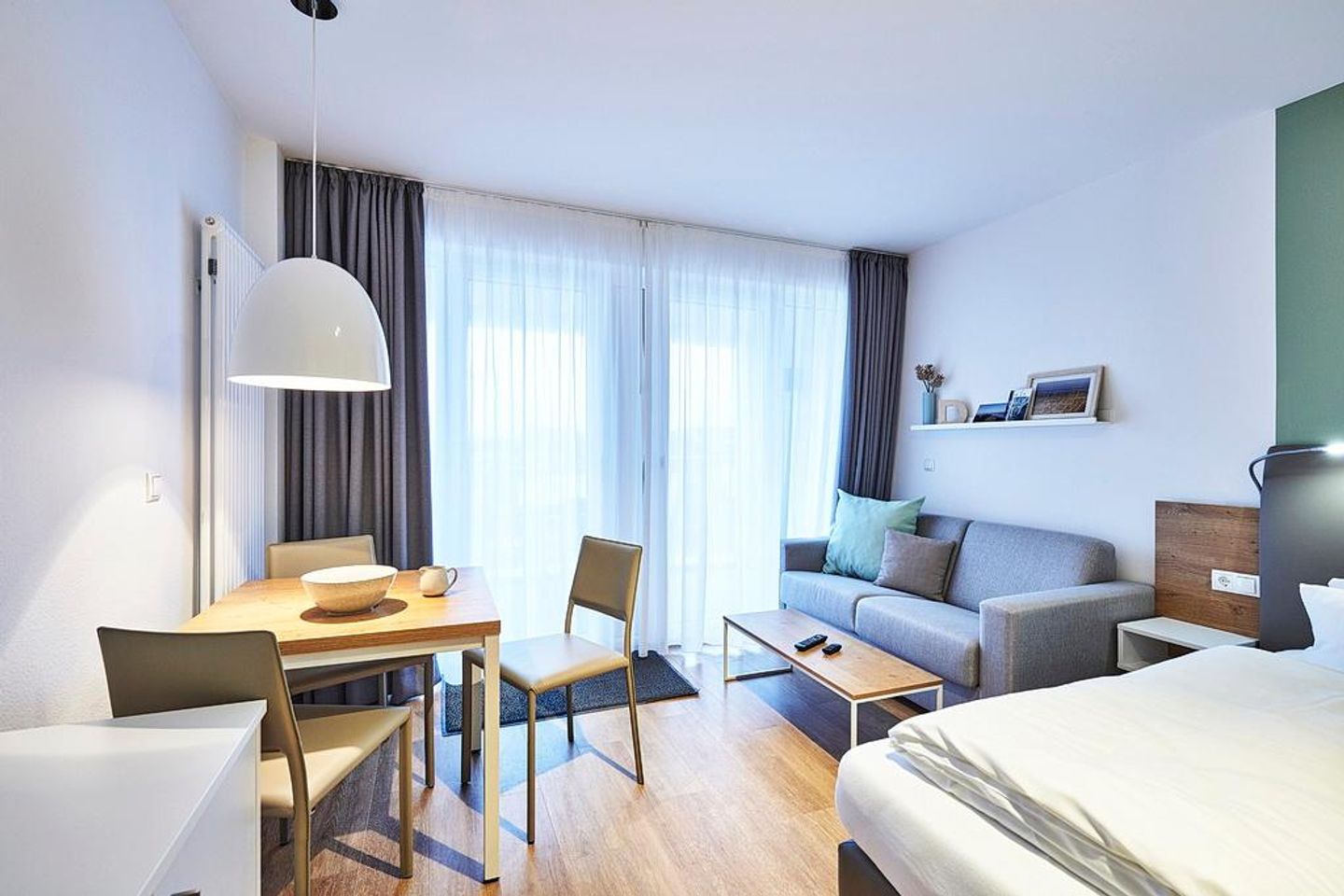 Deichhäuser Anna Küste Deichhäuser Anna Küste 4-22 Bensersiel - Wohn-Ess-Schlafbereich mit Sofa, Esstisch, Sitzgelegenheit und Doppelbett sowie Zugang zum Balkon