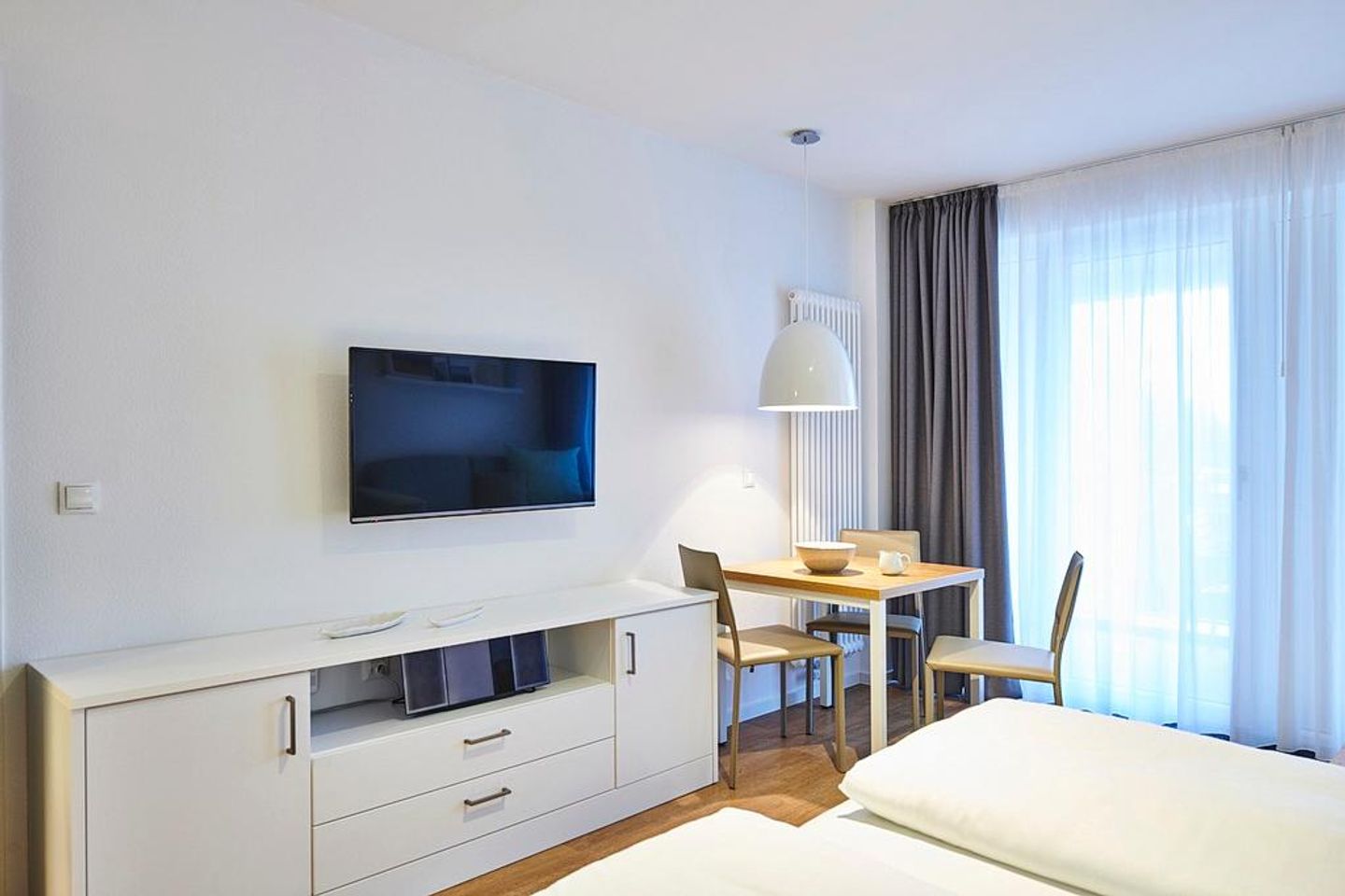 Deichhäuser Anna Küste Deichhäuser Anna Küste 4-22 Bensersiel - Wohn-Ess-Schlafbereich mit Sofa, Esstisch, Sitzgelegenheit und Doppelbett sowie Zugang zum Balkon