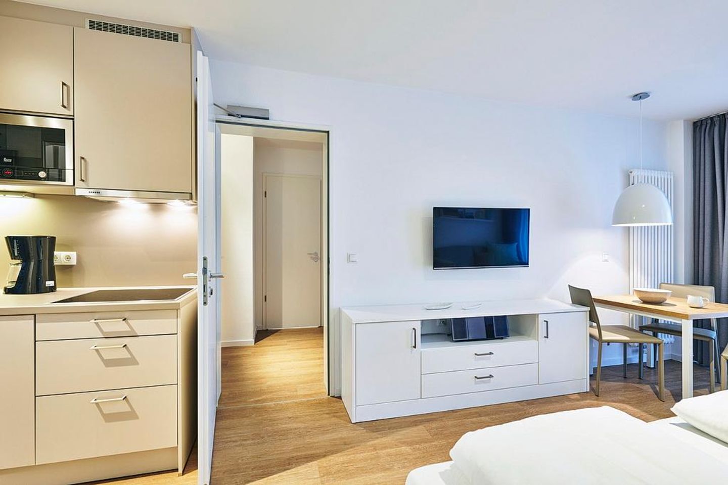 Deichhäuser Anna Küste Deichhäuser Anna Küste 4-22 Bensersiel - Wohn-Ess-Schlafbereich mit Sofa, Esstisch, Sitzgelegenheit und Doppelbett sowie Zugang zum Balkon