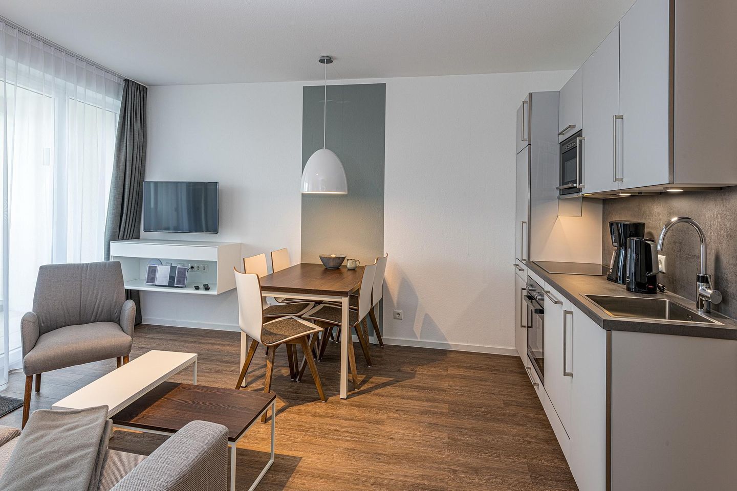 Deichhäuser Anna Küste Deichhäuser Anna Küste 7-21 Bensersiel - Wohn-Essbereich mit Faltscreen TV, Esstisch, Sitzgelegenheit und Küchenzeile