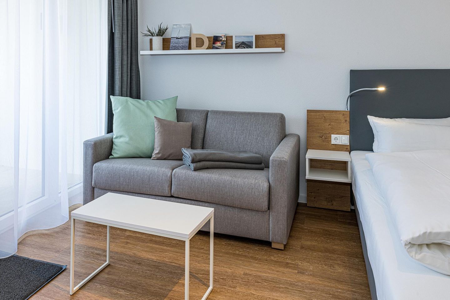 Deichhäuser Anna Küste Deichhäuser Anna Küste 8-22 Bensersiel - Wohn-Ess-Schlafbereich mit Sofa, Esstisch, Sitzgelegenheit und Doppelbett sowie Zugang zum Balkon