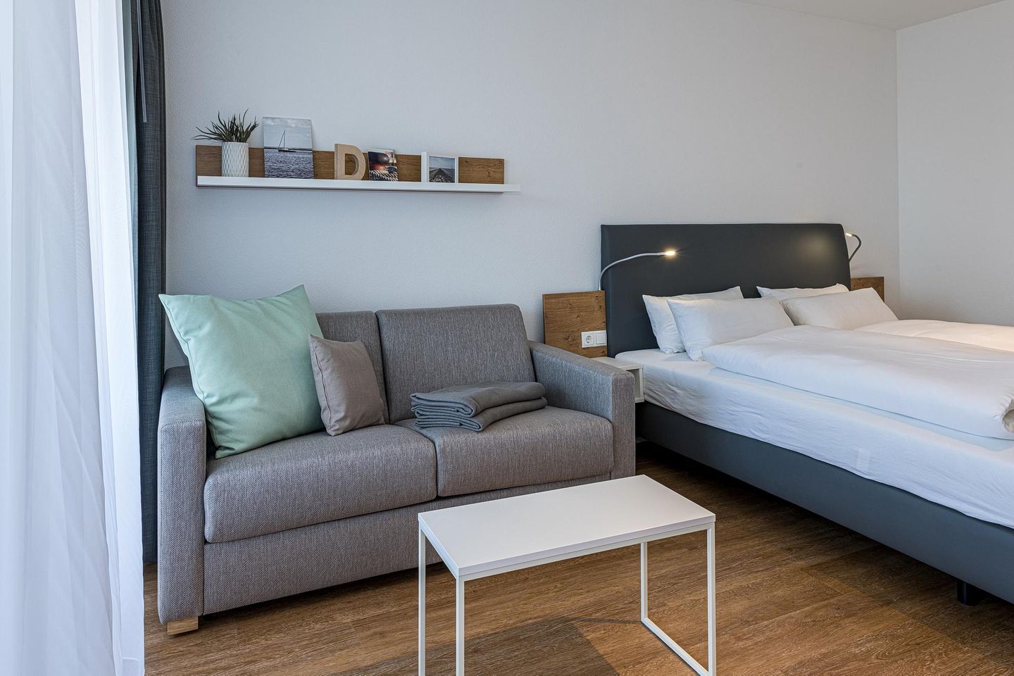 Deichhäuser Anna Küste Deichhäuser Anna Küste 8-22 Bensersiel - Wohn-Ess-Schlafbereich mit Sofa, Esstisch, Sitzgelegenheit und Doppelbett sowie Zugang zum Balkon