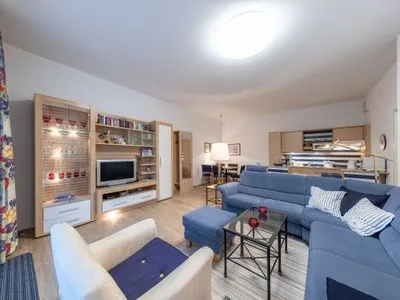 Ferienwohnung Bernstein Zingst – Großzügiges Wohnzimmer mit blauer Eckcouch, Vitrine, TV-Wand und offener Küche  Bernstein