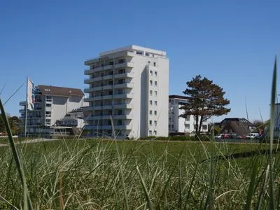Hohe Gräser vor dem Gebäude Pacific Duhnen, das eine exponierte Lage am Strand von Cuxhaven mit Meerblick hat. Haus Pacific Duhnen Nr. 91