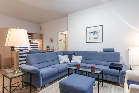 Ferienwohnung Bernstein Zingst – Gemütliches Wohnzimmer mit großer blauer Eckcouch, Glas-Couchtischen und maritimer Deko  Bernstein