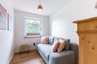  Boddenblick 1 Born auf dem Darß - Kleines Zimmer mit grauem Sofa, rosa Kissen, Holzschrank und Fensterblick.