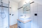  Boddenblick 1 Born auf dem Darß - Modernes Bad mit Dusche, Waschbecken, Spiegel und weiß gefliesten Wänden.