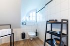  Boddenblick 1 Born auf dem Darß - Badezimmer mit Toilette, kleinem Fenster, Handtuchhalter und schwarzem Regal.