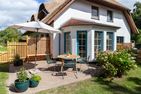 Boddenblick 1 Born auf dem Darß - Reetgedecktes Haus mit Terrasse, Sonnenschirm, Sitzgruppe und blühenden Büschen.