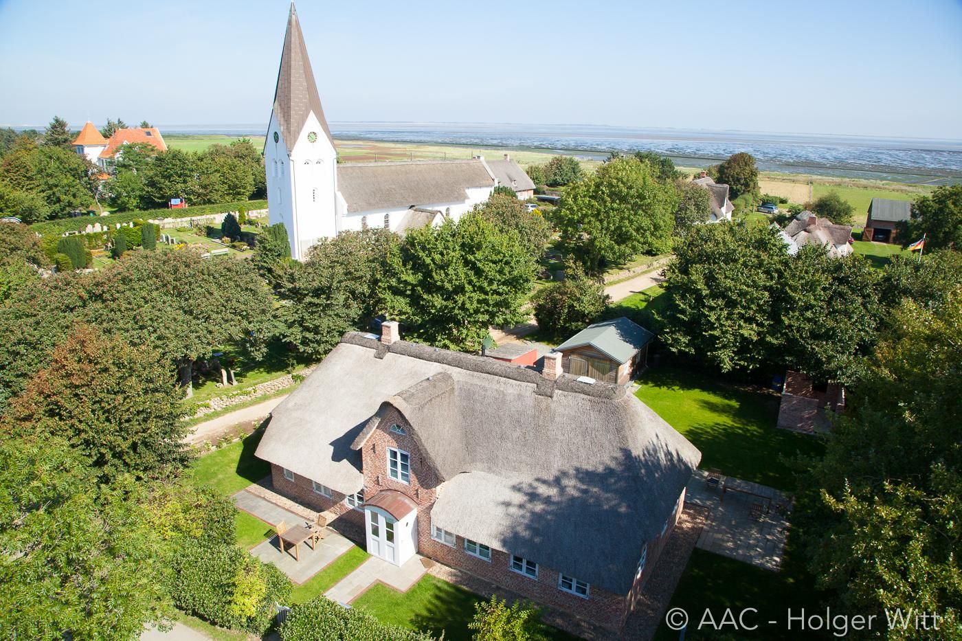Luftaufnahme von Nebel auf Amrum. Friesenhaus im Vordergrund, Kirche St Clemens im Hintergrund ist das Wattenmeer zu sehen.