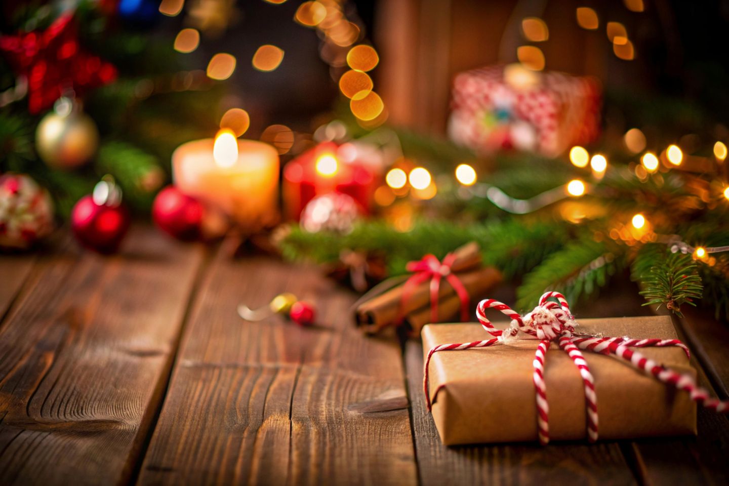 eingepacktes kleines Weihnachtsgeschenk vor Tannengrün und leuchtenden Kerzen