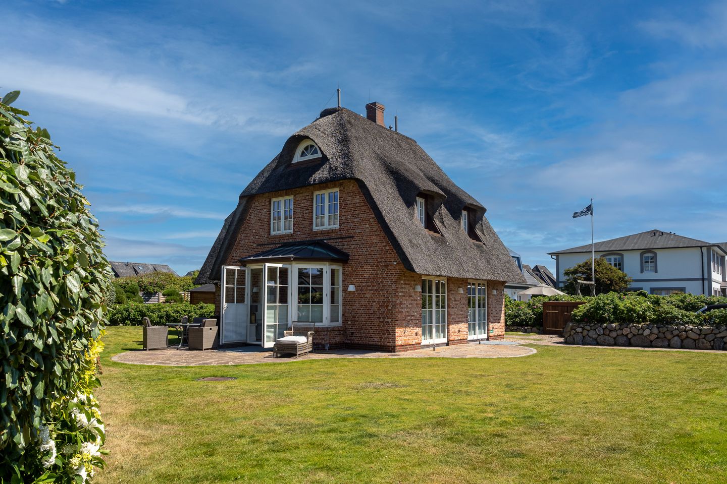ein mit Reet bedecktes Einzelhaus steht auf einem großen Grundstück mit Rasen und Friesenwall
