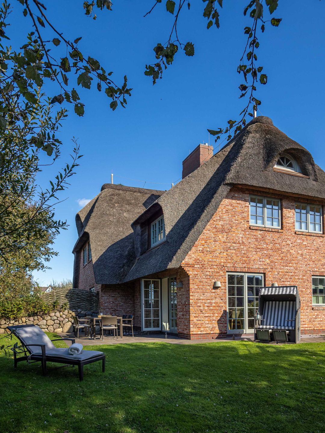 auf dem Rasen steht eine Liege mit Decke vor einem modernen Reetdachhaus in Wenningstedt