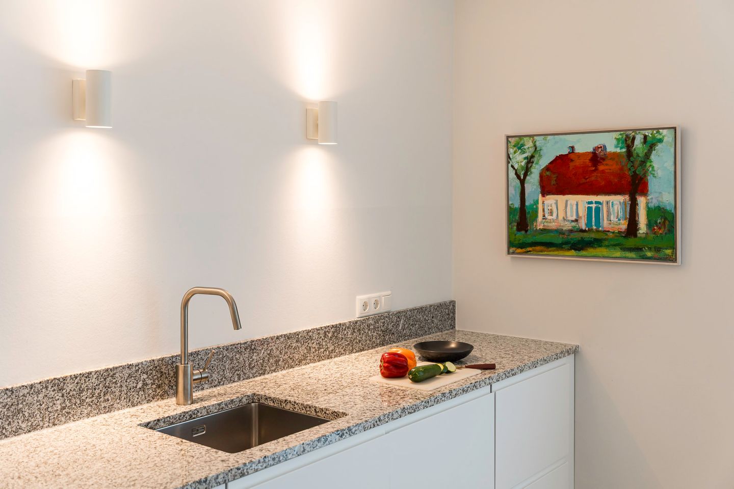 Küchenarbeitsplatte mit Brett und Gemüse, farbiges Bild an der Wand mit Haus