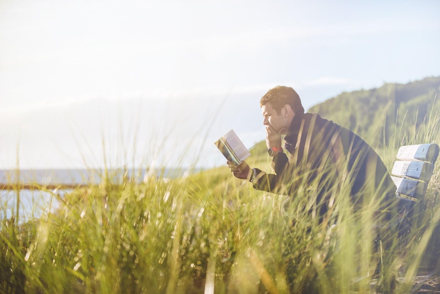 Mann sitzt im Strandgras und liest ein Buch