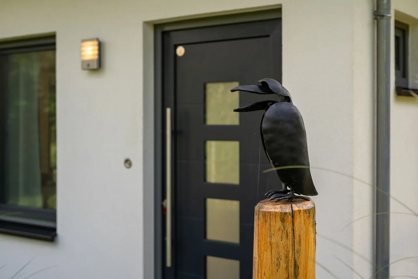 Kleine Sommerliebe Waren (Müritz) - Ferienhaus Kleine Sommerliebe Waren (Müritz) - Dekoratives Eingangselement mit Vogel-Skulptur und schwarzer Haustür