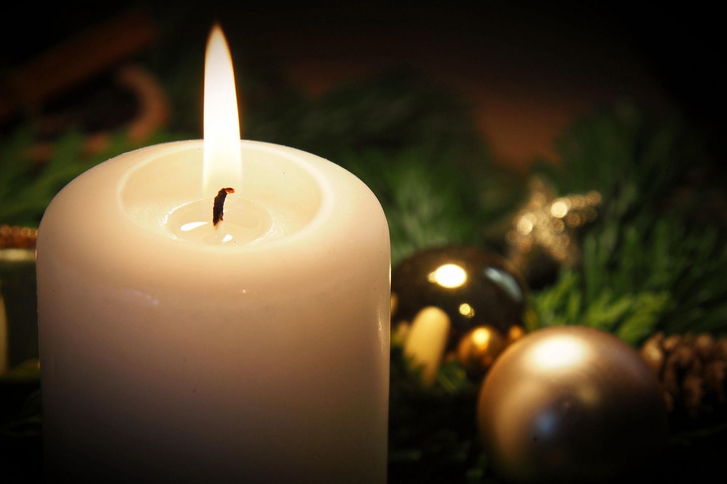 Erstes Adventslicht mit Tannengrün und goldenen Kugeln im Hintergrund