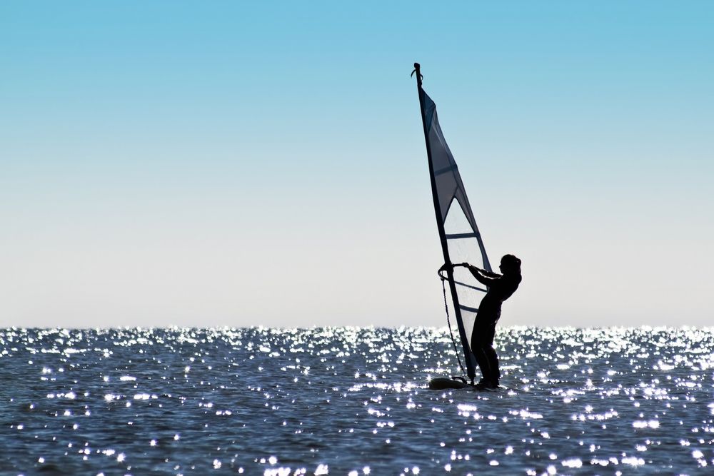 Frau beim Surfen auf der Ostsee bei blauem Himmel und flachen Wasser