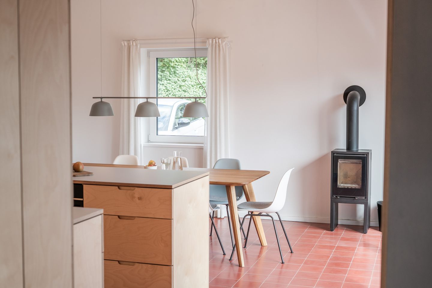 Blick in die puritisch eingerichtete Küche im Ferienhaus Seemannshaus Born - Holztisch mit Stühlen, weiße Fenster