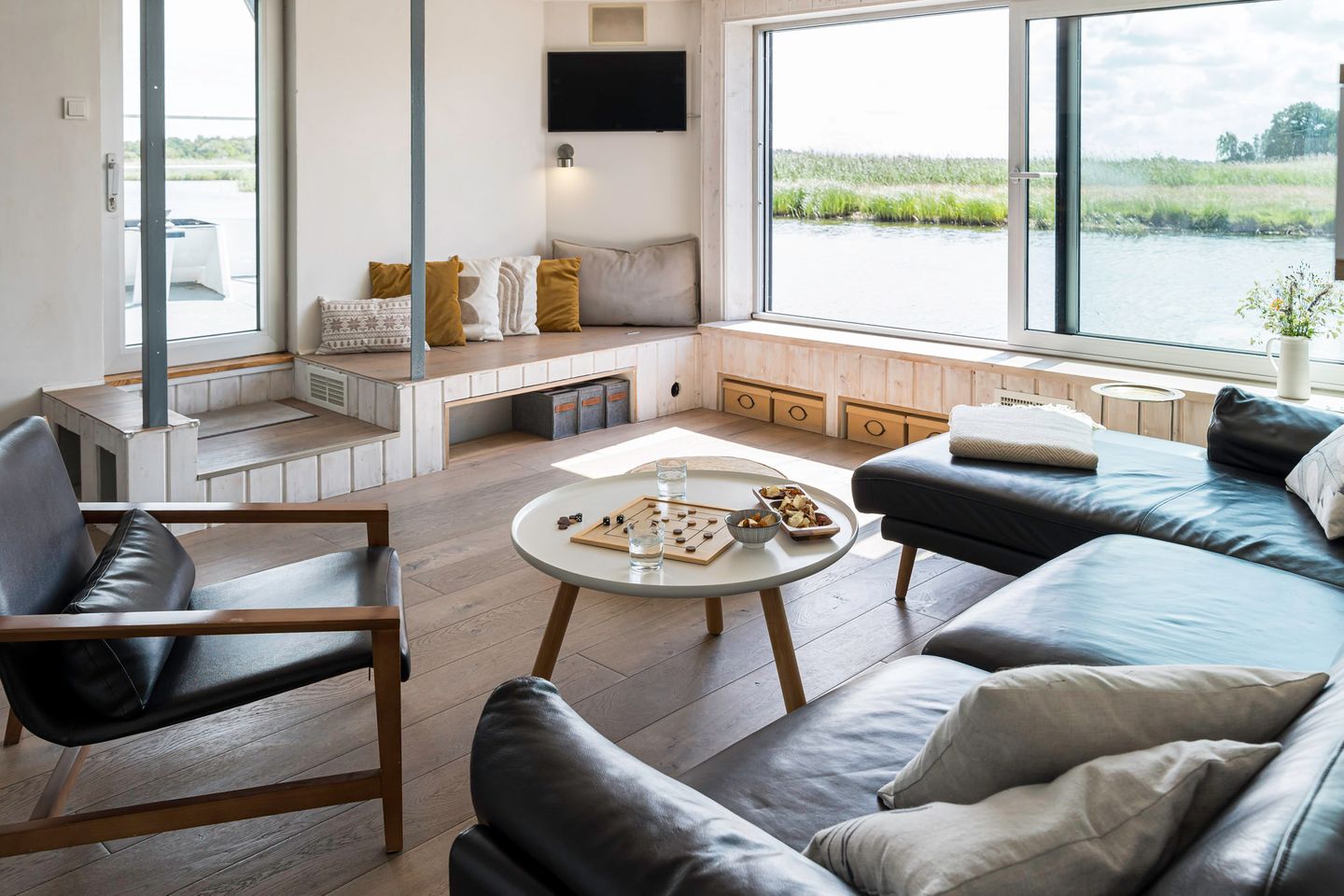 Blick ins Wohnzimmer mit Ledercouch und Ledersessel Wohnschiff Störtebecker, leicht geöffnetes Fenster, Blick auf das Wasser