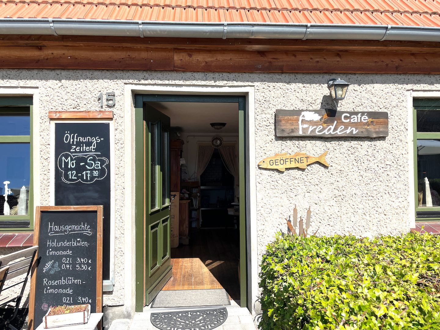 Hausansicht Cafe Freden in Wieck am Darß, Tür ist geöffnet, Schild mit Öffnungszeiten vor der Tür