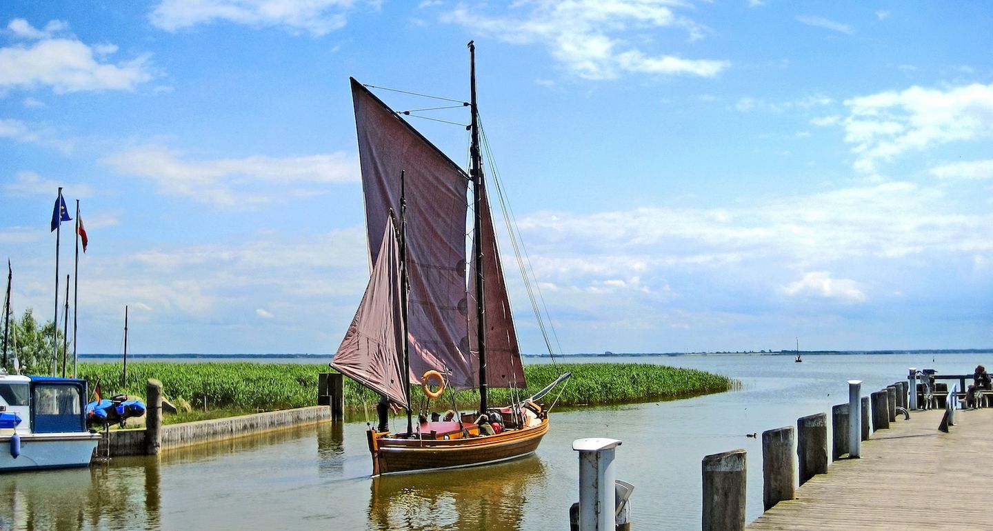 traditionelles Zeesboot mit braunen Segeln läuft in Hafen von Althagen bei Ahrenshoop ein, blauer Himmel mit Schäfchenwolken