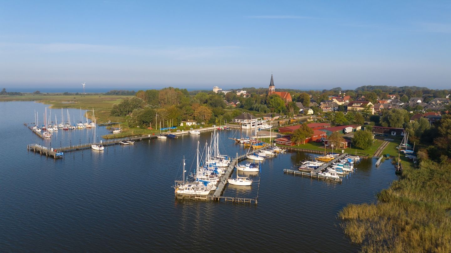Blick auf den Hafen von Wustrow aus der Vogelperspektive, Boote liegen im Wasser, blauer Himmel