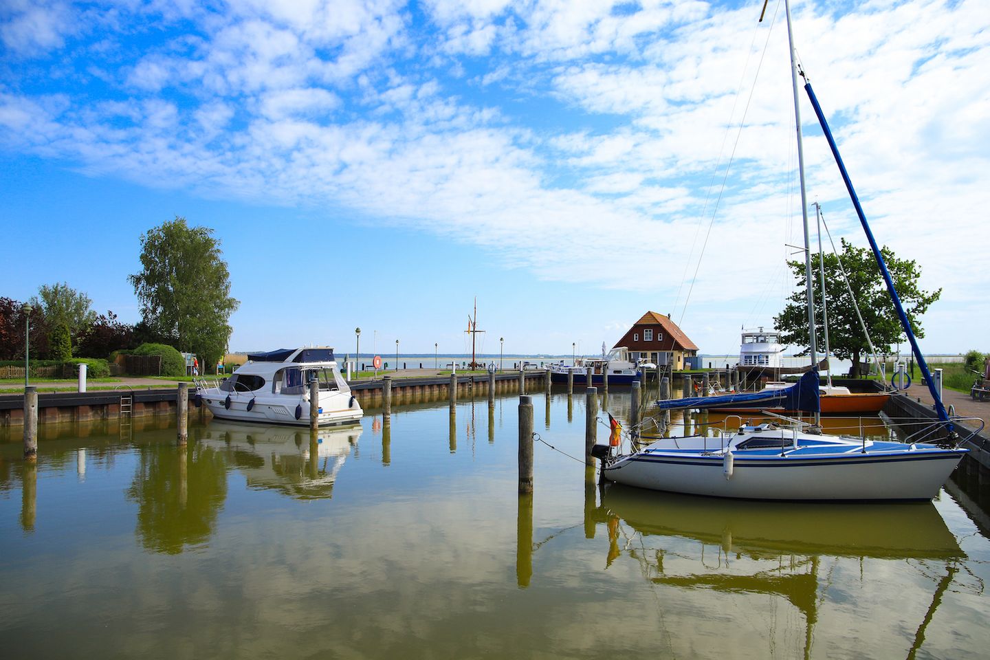 Blick auf den Hafen von Born am Darß, Schiffe liegen im Wasser, Kaimauer, Imbisshaus und Fähre im Hintergrund