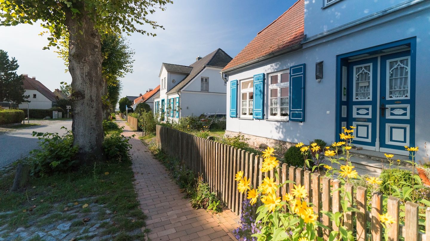 Blick auf Dorfstrasse in Wustrow mit altem Kapitänshaus mit blauen Fensterläden  und Linden vor dem Haus